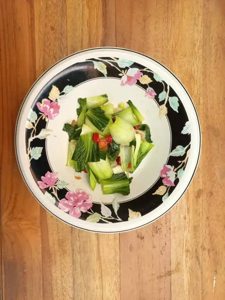 Tahta bir masanın üzerinde çiçek desenli bir kasede karıştırılmış Pak çikolatalı hardal yeşillikleri. Sebze yeme kavramı vücut sağlığı için iyidir. Yemek fotoğrafçılığı. Kapatın. Uzayı kopyala Seçici odak.