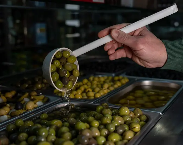 Elinde bir kaşık dolusu yeşil zeytinle markette