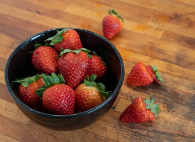 Ahşap bir arka planda siyah bir kasede çilek