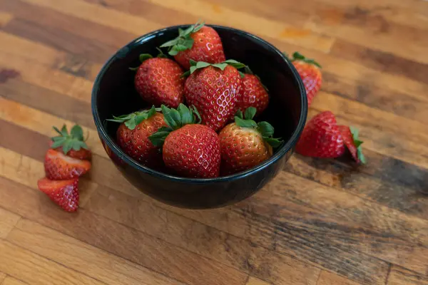 Tahta bir masanın üzerinde bir grup taze çilek olan siyah kase.
