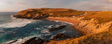 İspanya 'nın kuzeyinde gün batımında sahil ve kıyı şeridi. Kahverengi ve sarı çayır, büyük dalgalar ve kaya oluşumları