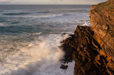 Cantabria 'nın ender kıyılarında, ilkbaharda gün batımında kayalara vuran dalgalar (İspanya)