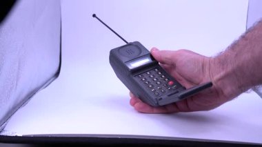 Beyaz arka planda eski bir analojik cep telefonunu kullanan bir adam.