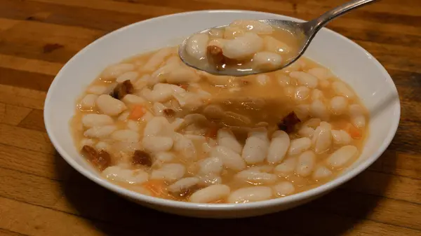 Geleneksel pişmiş beyaz fasulyeli beyaz tabak ve yemeye hazır bir kaşık. Akdeniz diyeti