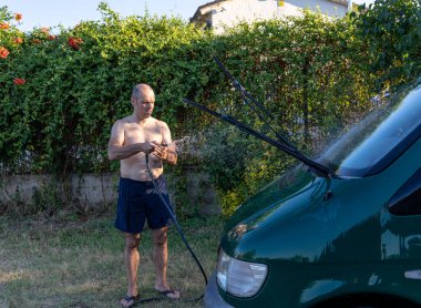 Yetişkin adam minibüsü yıkıyor ve hortumu ayarlıyor.