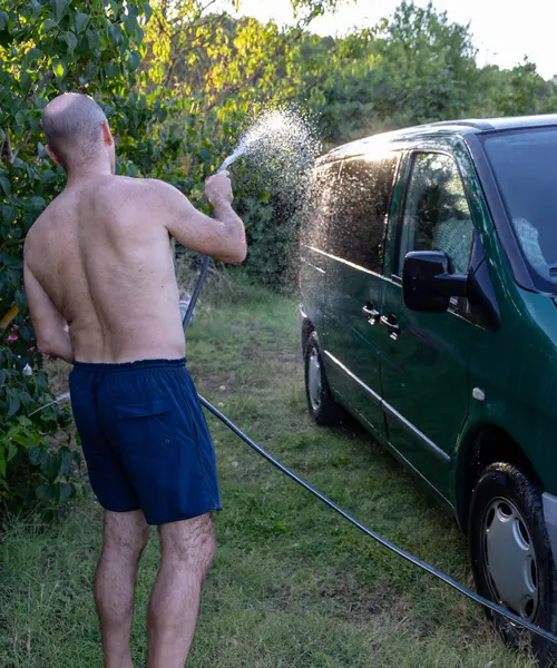 Bahçede hortumla arabasını yıkayan bir adam. Bakış açısı