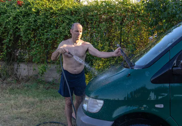 Yetişkin bir adam minibüsünü yıkıyor ve silecekleri tutuyor.