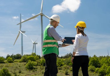 İki mühendis bir dizüstü bilgisayarla rüzgar türbini alanında çalışıyor.