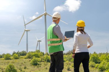 Bir kadın ve bir adam rüzgar türbinleri üzerinde çalışıyor.