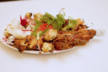 Sizzling Spice Sensation: Tandoori Chicken ve ağız sulandıran kebapların yer aldığı bir tabakta keyif çatmak, mis kokulu nane, turşu kokulu soğan halkaları ve gevrek lahana telleri ile süslenmiş, tat ve doku senfonisi vaat eden.