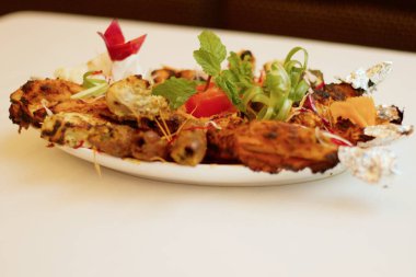 Sizzling Spice Sensation: Tandoori Chicken ve ağız sulandıran kebapların yer aldığı bir tabakta keyif çatmak, mis kokulu nane, turşu kokulu soğan halkaları ve gevrek lahana telleri ile süslenmiş, tat ve doku senfonisi vaat eden.