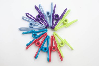 Başlık: Beyaz Arkaplanda Dairesel Desendeki Renkli Clothespinler. Temiz beyaz arkaplana karşı dairesel ve dairesel desenli olarak düzenlenmiş renkli plastik mandalların canlı tepeden aşağı görüntüsü.. 