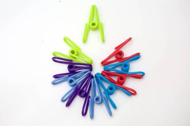 Renkli plastik mandallardan oluşan canlı bir tepeden tırnağa resim. Temiz beyaz bir arkaplanda dairesel bir desen oluşturulmuş. Simetrik düzen ve gökkuşağı renkleri, kavramlara uygun, görsel olarak çekici minimum bir kompozisyon oluşturur..