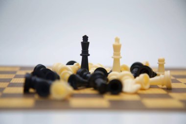 Bir satranç tahtası, kalan iki papazın etrafını saran sayısız düşen taşlarla dolu dramatik bir satranç oyunu sahnesi sergiliyor. İki kral, kaosun ortasında, görüntünün merkezine yakın bir yerde dururlar.. 