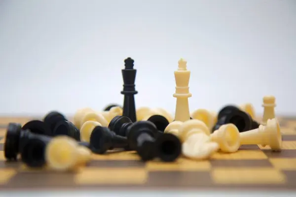 Oyunun son anlarını gösteren bir satranç tahtasının yakından çekimi. Düşen parçalar ve ayakta duran krallar stratejik karar verme mekanizmasını ve zafere ulaşma planının önemini vurguluyor..