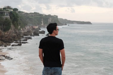 Maceraperest Kaşif Engebeli bir sahil manzarasında okyanusun kenarında duruyor.