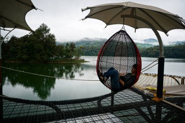 Gölün kenarındaki sallanan bir hamakta dinlenen adam, Lembang 'taki doğa inzivası.