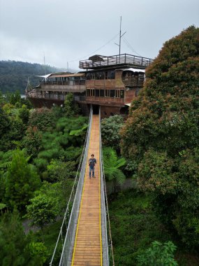 Male Asian Tourist Standing on Bridge to Wooden Ship Restaurant, Aerial View clipart