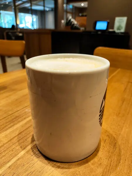 stock image Warm Cup of Cappucino Coffee in a Coffee Mug on Wooden Table in Cozy Cafe