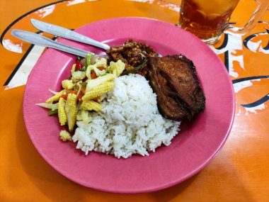 Beyaz pirinç, baharatlı tempeh, sotelenmiş sebze ve pembe bir tabakta sunulan ve özgün Endonezya aromalı kızarmış tofu içeren lezzetli warteg yemeği.