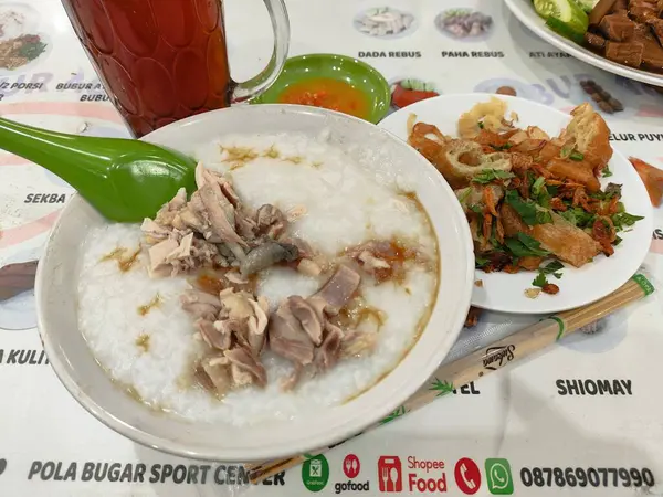 Üstünde et ve sebze olan bir kase beyaz yulaf lapası. Kase bir kaşık ve bir bardak çayla bir masanın üzerinde.