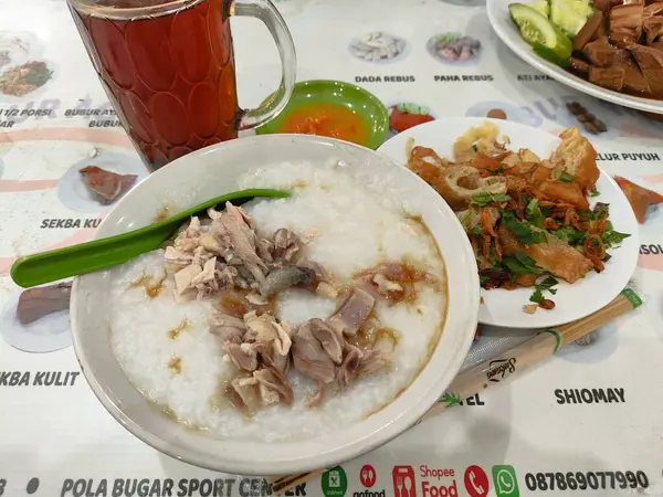 Üstünde et ve sebze olan bir kase beyaz yulaf lapası. Kase bir kaşık ve bir bardak çayla bir masanın üzerinde.