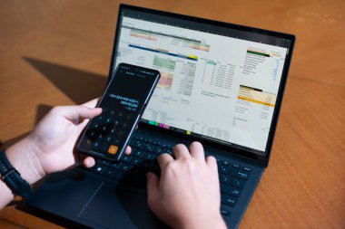 Temiz bir çalışma alanı üzerinde bir bütçe uygulaması ve hesap makinesi kullanarak kişisel finansman yöneten bir kişinin omuz üstü çekimi..