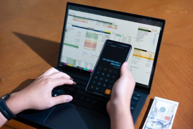 Temiz bir çalışma alanı üzerinde bir bütçe uygulaması ve hesap makinesi kullanarak kişisel finansman yöneten bir kişinin omuz üstü çekimi..