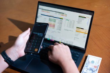 Temiz bir çalışma alanı üzerinde bir bütçe uygulaması ve hesap makinesi kullanarak kişisel finansman yöneten bir kişinin omuz üstü çekimi..