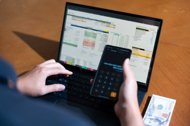 Temiz bir çalışma alanı üzerinde bir bütçe uygulaması ve hesap makinesi kullanarak kişisel finansman yöneten bir kişinin omuz üstü çekimi..