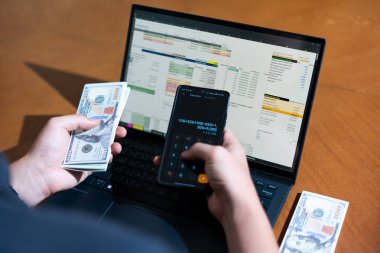 Temiz bir çalışma alanı üzerinde bir bütçe uygulaması ve hesap makinesi kullanarak kişisel finansman yöneten bir kişinin omuz üstü çekimi..