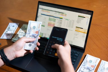 Temiz bir çalışma alanı üzerinde bir bütçe uygulaması ve hesap makinesi kullanarak kişisel finansman yöneten bir kişinin omuz üstü çekimi..