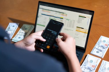 Temiz bir çalışma alanı üzerinde bir bütçe uygulaması ve hesap makinesi kullanarak kişisel finansman yöneten bir kişinin omuz üstü çekimi..