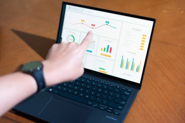 Bir kişi üzerinde grafik olan bir dizüstü bilgisayarı işaret ediyor. Grafik bir düşüş eğilimi gösteriyor, bu da satışlarda bir düşüş ya da olumsuz bir sonuç anlamına gelebilir.