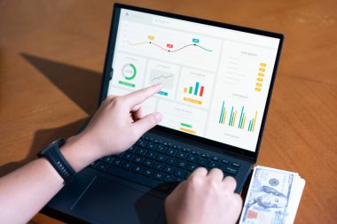 Bir kişi üzerinde grafik olan bir dizüstü bilgisayarı işaret ediyor. Grafikte yükselen bir eğilim var, bu da satışlarda bir artış ya da olumlu bir sonuç anlamına gelebilir.