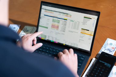 Temiz bir çalışma alanı üzerinde bir bütçe uygulaması ve hesap makinesi kullanarak kişisel finansman yöneten bir kişinin omuz üstü çekimi..