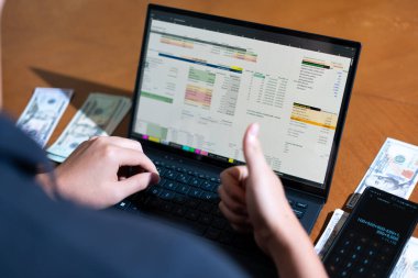 Temiz bir çalışma alanı üzerinde bir bütçe uygulaması ve hesap makinesi kullanarak kişisel finansman yöneten bir kişinin omuz üstü çekimi..