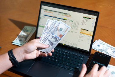 Bir kişi dizüstü bilgisayar ve bir yığın para tutuyor. Kişi muhtemelen dizüstü bilgisayarını mali işlerini yönetmek ya da satın almak için kullanıyor. Mali sorumluluk kavramı