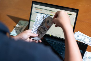 Bir kişi dizüstü bilgisayar ve bir yığın para tutuyor. Kişi muhtemelen dizüstü bilgisayarını mali işlerini yönetmek ya da satın almak için kullanıyor. Mali sorumluluk kavramı