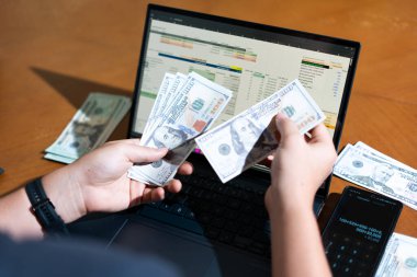 Bir kişi dizüstü bilgisayar ve bir yığın para tutuyor. Kişi muhtemelen dizüstü bilgisayarını mali işlerini yönetmek ya da satın almak için kullanıyor. Mali sorumluluk kavramı