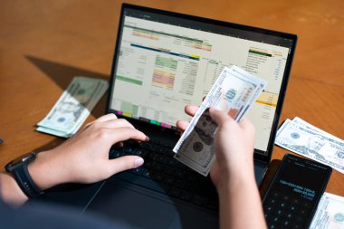 Bir kişi dizüstü bilgisayar ve bir yığın para tutuyor. Kişi muhtemelen dizüstü bilgisayarını mali işlerini yönetmek ya da satın almak için kullanıyor. Mali sorumluluk kavramı