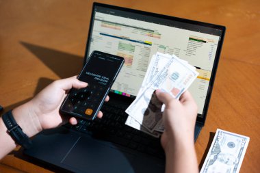 Temiz bir çalışma alanı üzerinde bir bütçe uygulaması ve hesap makinesi kullanarak kişisel finansman yöneten bir kişinin omuz üstü çekimi..