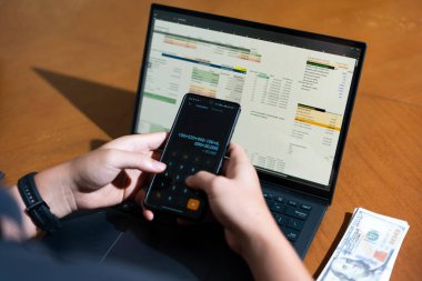 Temiz bir çalışma alanı üzerinde bir bütçe uygulaması ve hesap makinesi kullanarak kişisel finansman yöneten bir kişinin omuz üstü çekimi..