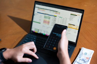 Temiz bir çalışma alanı üzerinde bir bütçe uygulaması ve hesap makinesi kullanarak kişisel finansman yöneten bir kişinin omuz üstü çekimi..