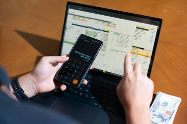 Temiz bir çalışma alanı üzerinde bir bütçe uygulaması ve hesap makinesi kullanarak kişisel finansman yöneten bir kişinin omuz üstü çekimi..