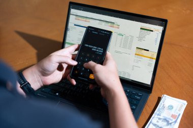 Temiz bir çalışma alanı üzerinde bir bütçe uygulaması ve hesap makinesi kullanarak kişisel finansman yöneten bir kişinin omuz üstü çekimi..