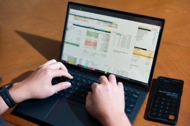 Temiz bir çalışma alanı üzerinde bir bütçe uygulaması ve hesap makinesi kullanarak kişisel finansman yöneten bir kişinin omuz üstü çekimi..