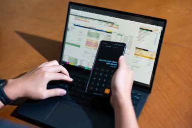 Temiz bir çalışma alanı üzerinde bir bütçe uygulaması ve hesap makinesi kullanarak kişisel finansman yöneten bir kişinin omuz üstü çekimi..