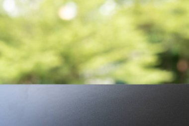 Ön planda yeşil ağaç yapraklarının yumuşak odaklı arka planına sahip temiz, boş bir masa üstü veya ekran panosu bulunan minimalist resim. Ürün modelleri, sunumlar veya dizayn şablonları için ideal.