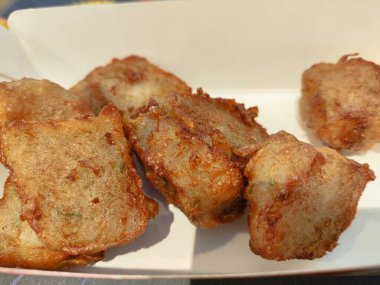 Bir tepsi kızarmış siomay yemeği ve beyaz bir kap. Yemekler kızarmış ve lezzetli görünüyor. Konteynır beyaz ve dikdörtgen şeklinde.